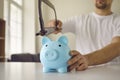 Strange young man needs money and is going to cut through his piggy bank with a saw Royalty Free Stock Photo