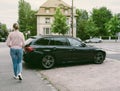 Casual French woman walking past a black luxury BMW wagon