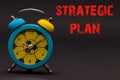 Strategic Plan written with alarm clock on black paper background