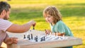 strategic and tactic. tutorship. dad and kid play logic game. father and son playing chess outside