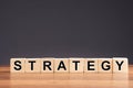 Strategy word written on cube shape wooden blocks on wooden table with a gray background.
