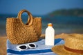 Straw bag, sunscreen bottle, hat, and white sunglasses laid out on blue towel by the sea for skin safety and style on Royalty Free Stock Photo