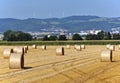 Straw bales in the field with the city and wind turbines in the background.