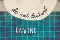 Straw hat with Do not disturb wording at the pool edge with Unwind... wording