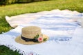 Straw hat with fresh flowers lay on a white picnic blanket at green lawn bright summer day background. Summer weekends leisure Royalty Free Stock Photo