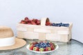 A straw hat, fresh strawberries and blueberries lie in a plate and basket on a glass table against the background of a plastered Royalty Free Stock Photo