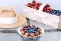 A straw hat, fresh strawberries and blueberries lie in a plate and basket on a glass table against the background of a plastered Royalty Free Stock Photo