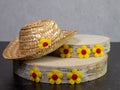 Straw hat on top of birch tree pieces of wood decorated with yellow flowers with dark pink centers sitting against a black slate