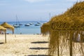 Straw parasols on a sandy beach with a yachts sailing on the background Royalty Free Stock Photo