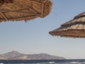 Straw Roof Of Beach Umbrella And Blue Sky, Mountain With Ocean In Background. Beach Vacation And Travel Concept Royalty Free Stock Photo