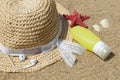 Straw sun hat, earphones, a bottle of sunscreen and a starfish on beach sand.