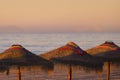 Straw umbrellas with multi-colored capes on an empty sandy beach in the rays of a golden sunrise.