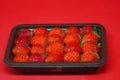 Strawberries arranged in rows in black plastic plate on the red background