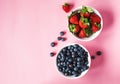 Strawberries and blueberries in bowls on pink background