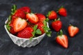 Strawberries in a bowl showing fresh ripe whole and cut in half strawberry fruits in a white bowl on dark background Royalty Free Stock Photo