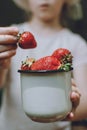 Strawberries in children hands. Girl child holding fresh red organic strawberries in white enameled cup. Summer vitamins