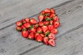 Strawberries cut in half, arranged to shape of heart, placed on gray wood desk