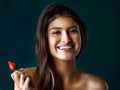 Strawberries are delicious. Portrait of a gorgeous young woman holding a strawberry against a dark background.