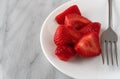 Strawberries and a fork on a white plate atop a marble counter top Royalty Free Stock Photo