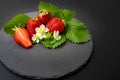 Strawberries on green leaves and white flowers, on a round black stone tile, isolated on black background. textures Royalty Free Stock Photo