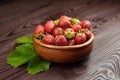 Strawberries with green leaves in wooden bowl on brown table. Red ripe berries, fresh juicy strawberries on wooden background Royalty Free Stock Photo