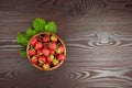 Strawberries with green leaves in wooden bowl on table, top view. Red ripe berries, fresh juicy strawberry on wooden background Royalty Free Stock Photo