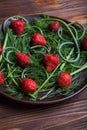 Strawberries and greens on a brown plate on wooden background. Royalty Free Stock Photo
