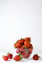 Strawberries lie in a glass transparent bowl and on a white wooden table on a white background. Royalty Free Stock Photo