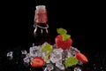 Strawberries, mint leaves, ice cubes and a bottle of strawberry juice with drops of water on a black background Royalty Free Stock Photo