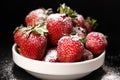 Strawberries in a plate with powdered sugar on a black background, side view close-up. Royalty Free Stock Photo