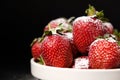 Strawberries in a plate with powdered sugar on a black background, side view close-up. Royalty Free Stock Photo