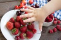 Strawberries, raspberries, cherries on table. child& x27;s hand reach