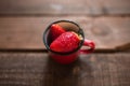 Strawberries in a red enamel mug on a wooden table
