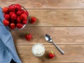 Strawberry in a bowl, whipped cream, teaspoon and linen napkin on brown wooden background.