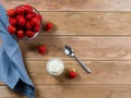Strawberry in a bowl, whipped cream, teaspoon and linen napkin on brown wooden background.