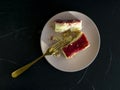 Strawberry cheesecake on a pink plate and a gold fork on a black textured background Royalty Free Stock Photo