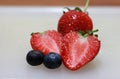 Strawberry and chopped strawberry with berry fruit on the white floor.