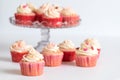 Strawberry cupcakes with cream cheese frosting on a cake stand with more on the table in front for Valentine`s Day.