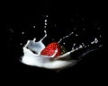 A strawberry falling down onto a spoon and splash into milk or cream - black background Royalty Free Stock Photo