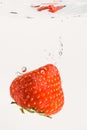 Strawberry falls deeply under water with a big splash. Fruit sinking in clear water on white background Royalty Free Stock Photo