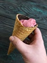 Strawberry ice cream in a waffle cone. In a manÃ¢â¬â¢s hand. Against the background of pine brushed boards painted in black and green Royalty Free Stock Photo