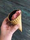 Strawberry ice cream in a waffle cone. In a manÃ¢â¬â¢s hand. Against the background of pine brushed boards painted in black and green Royalty Free Stock Photo