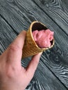 Strawberry ice cream in a waffle cone. In a manÃ¢â¬â¢s hand. Against the background of pine brushed boards painted in black and white Royalty Free Stock Photo