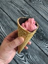 Strawberry ice cream in a waffle cone. In a manÃ¢â¬â¢s hand. Against the background of pine brushed boards painted in black and white Royalty Free Stock Photo
