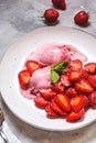 Strawberry ice cream in a white bowl with strawberries on a concrete background