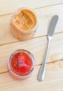 Strawberry jam and peanut butter on wooden table with butter knife