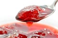 Strawberry jam is stirred with a spoon on a white background.
