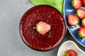 Strawberry marmalade in glass bowl with fresh berry half over grey concrete background Royalty Free Stock Photo