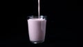 Strawberry milk shake isolated on black background. In transparent glass pour viscous pink milkshake on black background