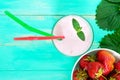 Strawberry-milkshake in a glass on a bright background among berries and green leaves.